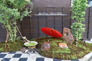 einen Garten mit einem roten Regenschirm und einigen Steinen in der Unterkunft Tabist Wa Style Tokyo in Kawaguchi