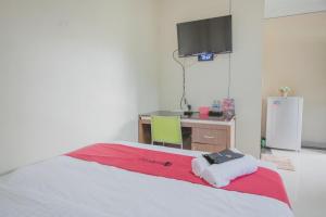 a bedroom with a bed with a desk and a tv at RedDoorz Syariah near Jamtos Jambi 2 in Jambi