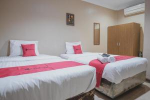 2 camas en una habitación con sábanas rojas y blancas en RedDoorz Syariah near Jamtos Jambi 2 en Jambi