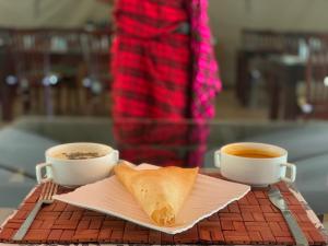 twee kopjes koffie en een stuk brood op een tafel bij Lorian safari camp limited in Narok