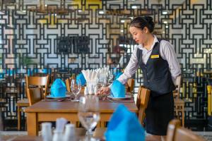 a woman is setting a table in a restaurant at Fivitel Hoi An Hotel in Hoi An