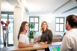 dos mujeres de pie en un mostrador hablando con un hombre en Schwan und Post Business Quarters en Bad Neustadt an der Saale