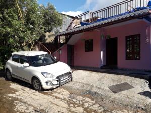 a white car parked in front of a pink house at Munnar Brindavan Cottage in Munnar