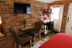 a room with a brick wall with a desk and a television at Boutique Garden Lodge @ The Larches in Wolverhampton