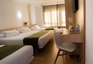 ミーニョにあるHotel Crisol de las Ríasのベッド3台、デスク、椅子が備わるホテルルームです。