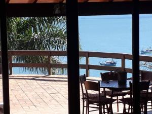 a table and chairs on a patio with a boat in the water at Luxury Suites Vila Indonésia in Garopaba