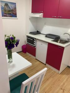 una pequeña cocina con armarios rojos y una mesa con un jarrón de flores en La Apartamento Centroom en Jagodina