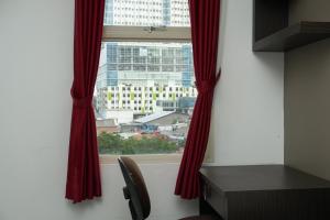 a window with red curtains and a desk and a chair at Elegant Studio Apartment at Margonda Residence 2 By Travelio in Depok