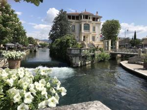 une vue d'une rivière avec un bâtiment et des fleurs dans l'établissement La Magnanerie, à LʼIsle-sur-la-Sorgue