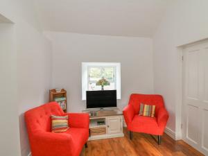 un soggiorno con 2 sedie rosse e una TV di The Old White Cottage a Shillelagh