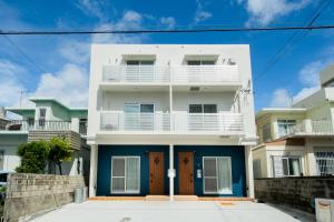 ペンション マカナレアビーチ沖縄 في غينوان: منزل أبيض وأزرق بأبواب زرقاء