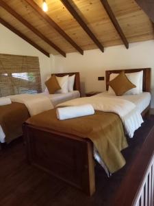 two beds in a room with wooden ceilings at 3Arch Eco Cottage Ella in Ella