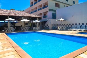 una piscina con sillas y sombrillas junto a un edificio en Thanharu Praia Hotel, en Anchieta