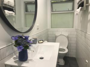 La salle de bains est pourvue d'un lavabo avec un vase de fleurs violettes. dans l'établissement Hahei Kereru Cottage, à Hahei