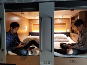 two people sitting on bunk beds reading books at Y's CABIN&HOTEL Naha Kokusai Street in Naha +82 photos