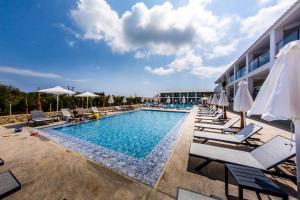 einen Pool mit Stühlen und Sonnenschirmen neben einem Hotel in der Unterkunft Caretta Paradise Resort & WaterPark in Tragaki