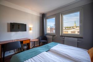 a bedroom with a bed and a desk and two windows at Enter Amalie Hotel in Tromsø