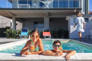 twee meisjes zitten in een zwembad met drankjes bij Terraces d'Orlando - Family Apartments with Sea View and Pool in Capo dʼOrlando