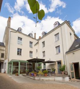 un grand bâtiment blanc avec des tables et des parasols dans l'établissement Logis Hôtel Le Vert Galant, à La Flèche