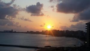einen Sonnenuntergang über dem Wasser mit einer Stadt in der Unterkunft Terraços, Frente Mar para o Atlântico in Fortaleza