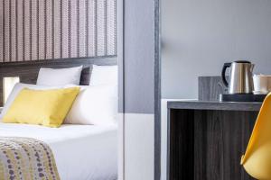 a bedroom with a bed with white sheets and yellow pillows at Best Western Portes d’Aquitaine Agen Sud in Le Passage