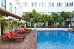 a pool with chairs and umbrellas next to a building at Mida Grande Hotel Dhavaravati Nakhon Pathom - SHA PLUS in Nakhon Pathom