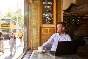 a man sitting at a table in a coffee shop with a laptop at Arlington Hotel O'Connell Bridge in Dublin