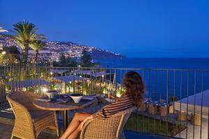 a woman sitting at a table looking out at the ocean at Les Suites at The Cliff Bay - PortoBay in Funchal