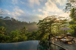 a pool with chairs and an umbrella and a view of the forest at Komaneka at Tanggayuda Ubud in Ubud