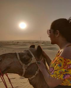 KūriにあるSunny Desert Campの浜辺のラクダの横に立つ女