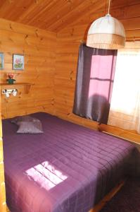 a purple bed in a wooden room with a window at Suvaksen Helmi in Kosula