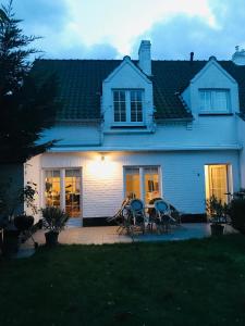 Casa blanca con sillas y mesa en el patio en Zee Vakantievilla Begijnhof 5 De Haan en Nieuwmunster