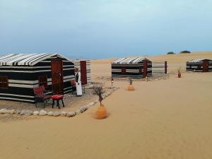 un hombre parado frente a dos tiendas en el desierto en Legend Desert camp, en Fulayj al Mashāʼikh