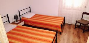 1 dormitorio con 2 camas con sábanas de color naranja y silla en Sa Domu Antiga en Solarussa