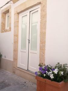 une porte blanche d'une maison avec des fleurs dans un pot dans l'établissement Judaica d'Ortigia, à Syracuse