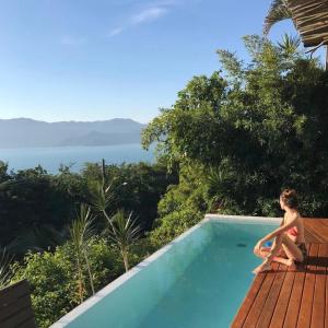 a woman sitting on the edge of a swimming pool at Villa Piccolo Di Mare in Ilhabela