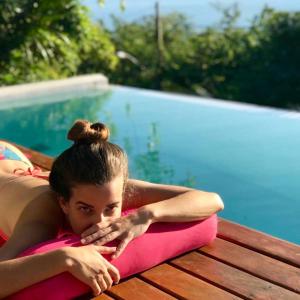 una mujer acostada en una almohada rosa junto a una piscina en Villa Piccolo Di Mare, en Ilhabela