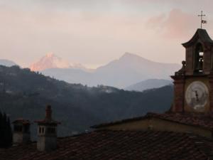 uma torre de relógio no topo de um edifício com uma montanha em Fattoria di Camporomano em Massarosa