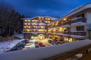 a hotel with cars parked in a parking lot in the snow at Perelik Hotel in Pamporovo