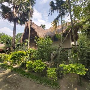 a house with a thatched roof and palm trees at MAHESWAR LAND in Majuli
