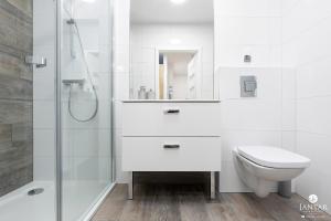 a white bathroom with a toilet and a shower at Jantar Apartamenty - Holiday Polanki Park SPA in Kołobrzeg