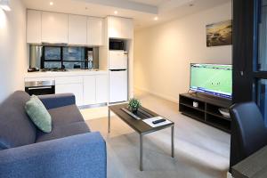 a living room with a couch and a tv and a kitchen at Flinders Street Apartments in Melbourne