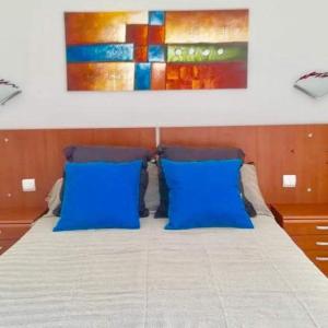 a bed with blue pillows and a painting on the wall at Appartement vue mer et soleil toute l année in Costa de Antigua
