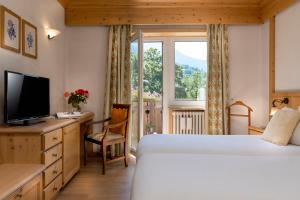 
a hotel room with a bed, tv and a window at Hotel Baita Dei Pini in Bormio
