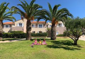 three girls sitting on the grass under palm trees at Marinos Apartments in Lassi