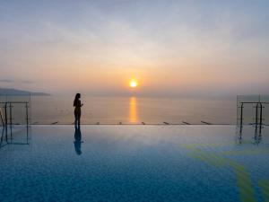 a woman standing on the edge of a pool looking at the sunset at Maximilan Danang Beach Hotel in Da Nang