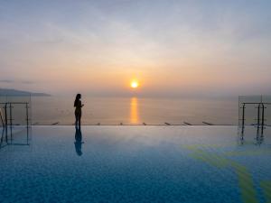 Una donna sul bordo di una piscina che guarda il tramonto di Maximilan Danang Beach Hotel a Da Nang