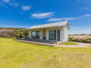 une petite maison avec une terrasse couverte sur une pelouse dans l'établissement Amhurst Cottage, à Port Fairy