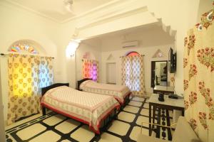 a bedroom with two beds and a table and windows at Chanod Haveli in Jodhpur