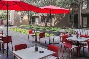 een patio met tafels en stoelen en rode parasols bij The Nicol Hotel Bedfordview in Johannesburg